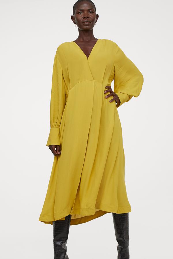 Este vestido midi en color amarillo y pronunciado escote de pico cuenta con puños anchos abotonados y falda con vuelo y pliegues. Tiene un precio de 49,99 euros.