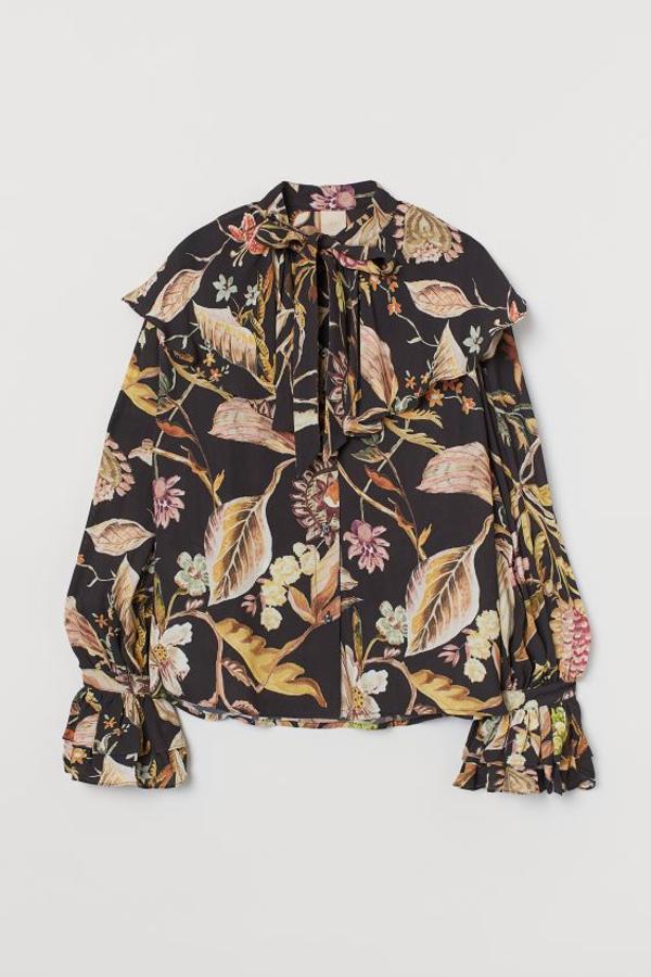 Esta blusa vaporosa de viscosa con cuello amplio voluminoso y tiras en el escote es de H&M y vienen con estampado floral en tonos marrones y rojizos sobre fondo negro. De corte amplio, con botones delante, mangas holgadas y tiras con volante doble en los puños, cuesta 39,99 euros y está disponible entre las tallas XS y XL.