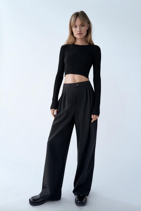 Con cierre frontal de botón y cremallera, este pantalón ancho de tiro alto de Zara es de color negro y viene con detalle de pliegues en delantero. Con bolsillos laterales, cuesta 25,95 euros y está disponible entre las tallas XS y L.