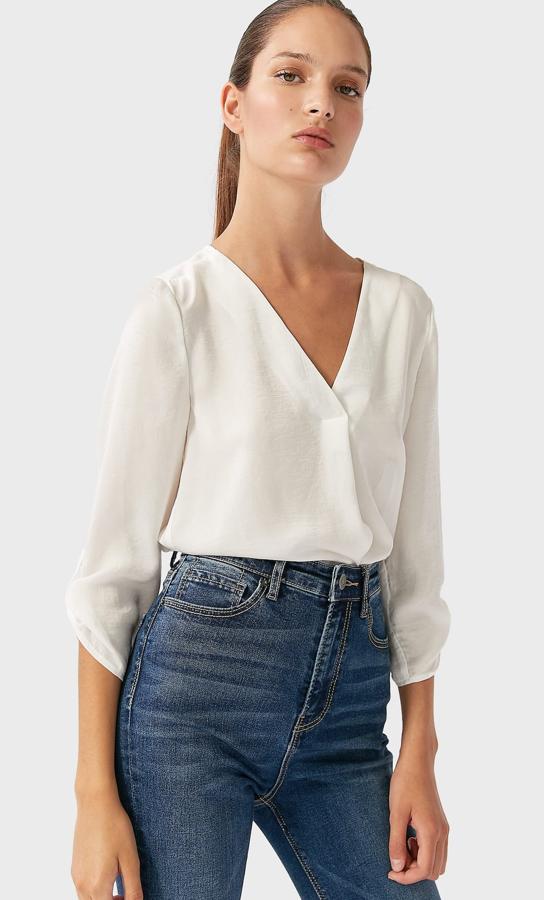 Esta camisa blanca de tejido fluido y escote de pico cuenta con manga tres cuartos y tiene un precio de 17,99 euros. Es de Stradivarius.