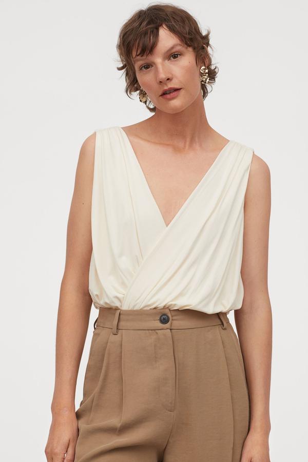 Diseño cruzado de punto con escote de pico pronunciado frontal y trasero para este body color crema de H&M. Con corte relajado con tirantes anchos y cintura entallada, tiene un precio de 14,99 euros y está disponible entre las tallas XS y XXL, y en negro.