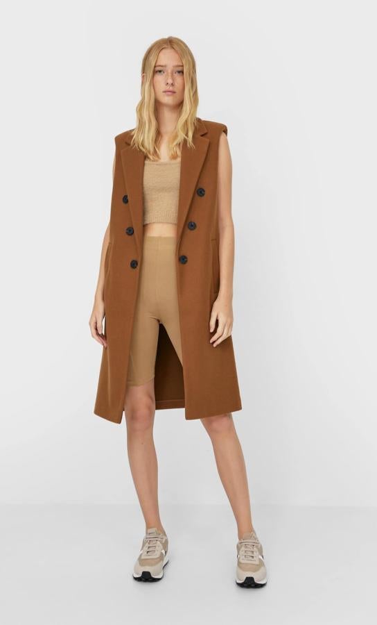 De cuello y solapa con manga sisa, este chaleco largo de Stradivarius en color marrón viene con bolsillos delanteros de vivo y cierre cruzado con botones a contraste en negro. Tiene un precio de 35,99 euros y está disponible entre las tallas XS y XL.