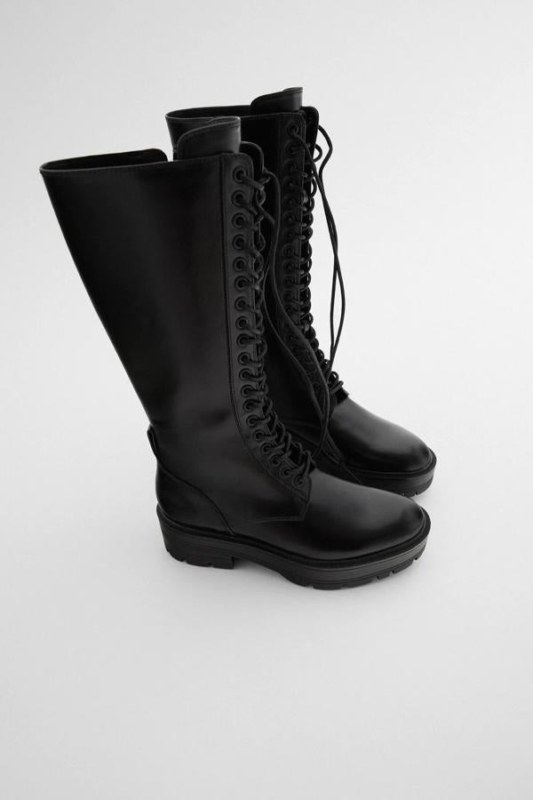 Esta bota alta plana en color negro cuenta con tirador en la parte trasera inferior y suela gruesa. Con cierre de cordones y cremallera interior, es de Zara y tiene un precio de 49,95 euros.