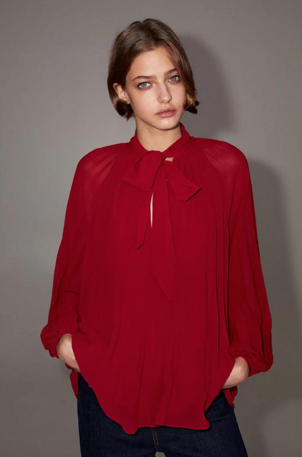 De cuello redondo con lazada y escote de pico, esta blusa plisada de Zara en color rojo viene con mangas largas acabadas en puño elástico. Cuesta 25,95 euros y está disponible entre las tallas XS y XXL.