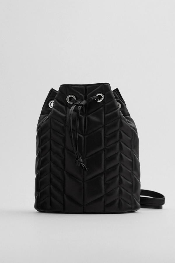 Este bolso formato mochila de color negro cuenta con cuerpo acolchado con pespuntes y asa de hombro ajustables de doble función. Con cierre mediante fruncido, tiene un precio de 29,95 euros.