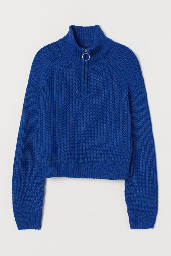En color azul, este jersey de punto con cuello alto y cremallera cuenta con cuello, puños y bajo en punto de canalé. Disponible también en beige, tiene un precio de 19,99 euros.
