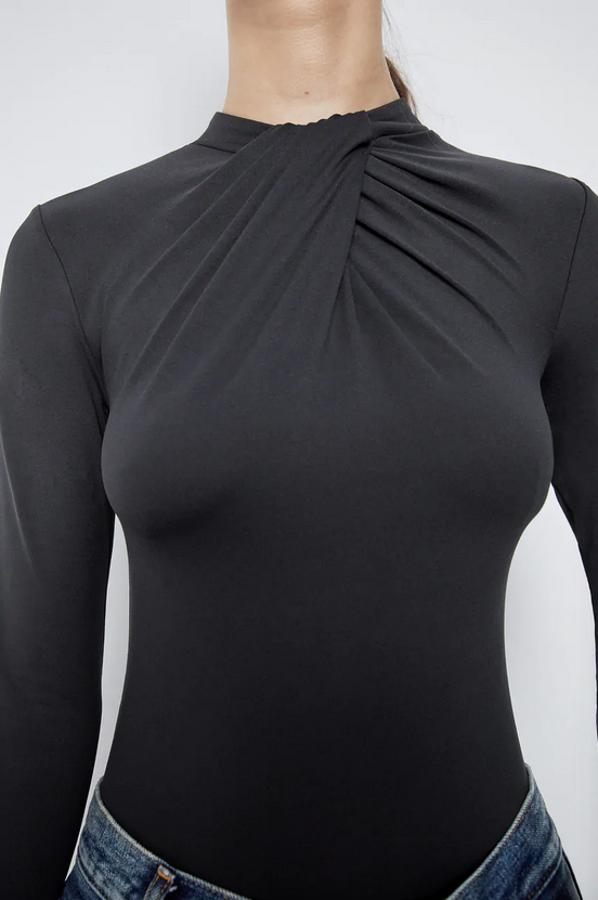 En mezcla de poliamida, este body ajustado de Zara con cuello redondo y manga larga en color negro viene con detalle de nudo en la parte del escote. Tiene un precio de 15,95 euros y está disponible en las tallas S, M y L.