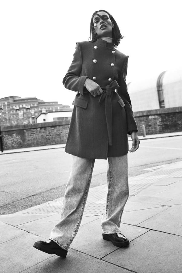 Cierre frontal cruzado con botones metálicos en dorado para este abrigo cruzado de Zara confeccionado con tejido en mezcla de lana y color caqui. Con cuello subido, mangas largas y hombros marcados, tiene bolsillos laterales con solapa y cinturón a tono y cuesta 69,95 euros. Está disponible entre las tallas XS y XXL.