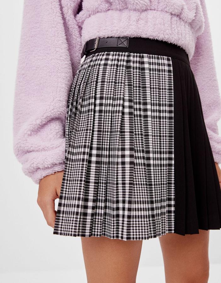 Diseño combinado para esta falda de tablas mini de Bershka con un lado en negro liso y otro con estampado de cuadros en negro y blanco. Cuesta 19,99 euros y está disponible entre las tallas XS y L.