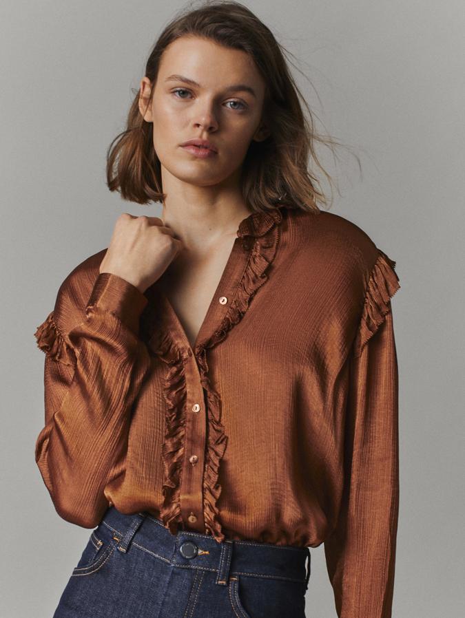 En color toffe, con volantes en los hombros, el cuello redondo y el escote, esta camisa con botonadura frontal a tono y puños abotonados, costaba 49,95 euros y está disponible entre las tallas 34 y 42 por 29,95 euros.