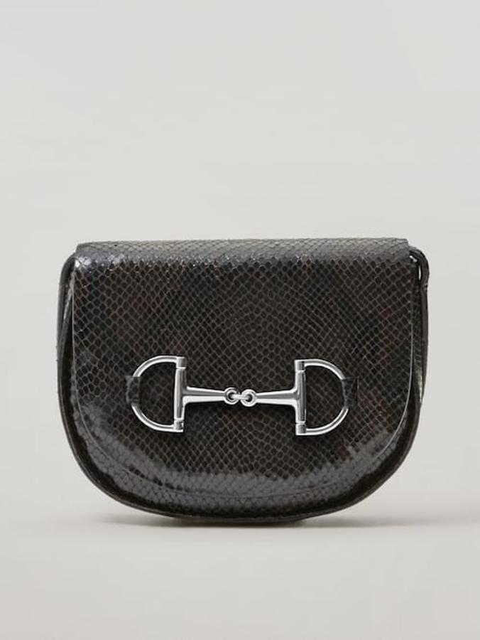 En marrón con efecto piel acharolado, esta bandolera confeccionada en piel caprina y bovina viene con correa de hombro ajustable y tiene un bolsillo interior. Con detalle de estribo en el frontal, cuesta 99,95 euros.