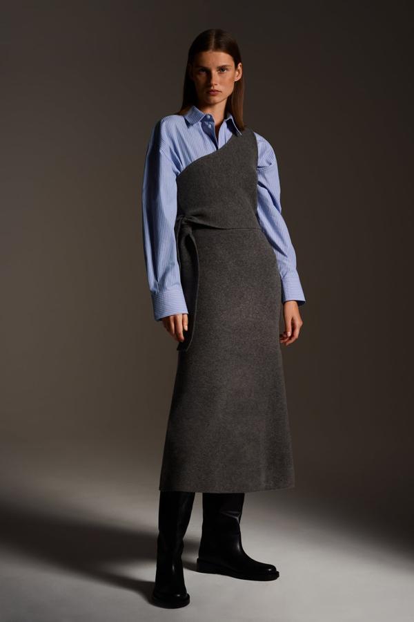 La sobriedad de un top asimétrico de punto y una falda a midi a juego no está reñido con superponerla a una camisa para hacer un original look de oficina, todo de Zara.