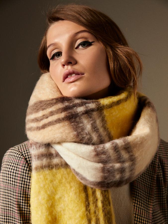 En amarillo y beige con cuadros en marrón, esta bufanda de tacto muy suave de Lefties con acabado en flecos cuesta 12, 99 euros.