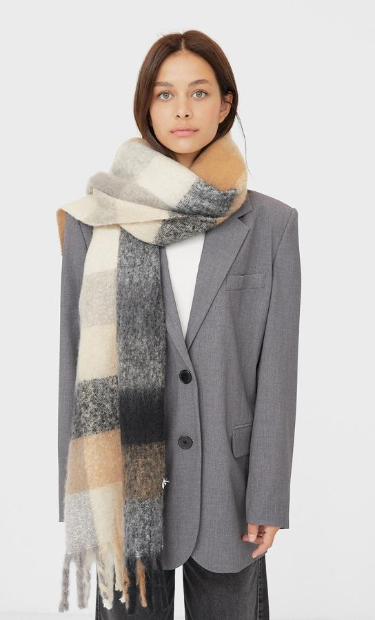 Flecos y estampado de cuadros en tonos beige, crudo y diferentes tonos de grises para esta bufanda de Stradivarius que tiene un precio de 15,99 euros.