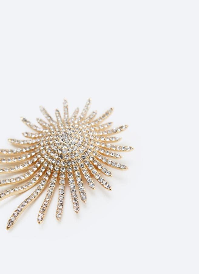 Con diseño tipo sol y cristales adornando toda la pieza, este broche de Uterqüe tiene un precio de 49 euros.