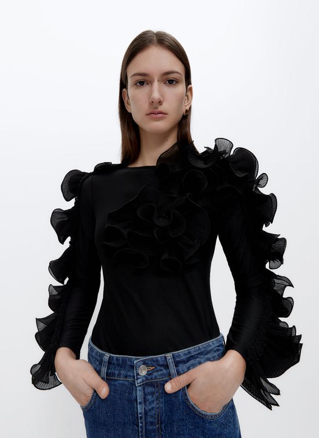Con cuello redondo y mangas largas con detalles de volantes plisados con tejido a contraste, esta camiseta negra viene con detalle de flores con tejido plisado en el frontal. Tiene un precio de 59 euros y está disponible en las tallas S, M y L.