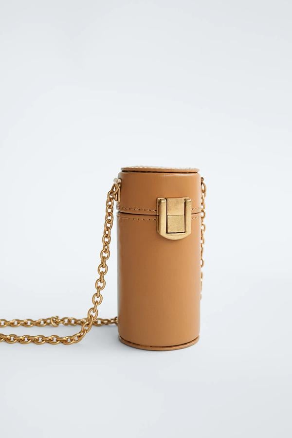 Este mini bolso con forma cilíndrica en color tostado cuenta con asa metálica de hombro y detalle de espejo en el interior. Es de Zara, está también disponible en color negro y tiene un precio de 12,95 euros.
