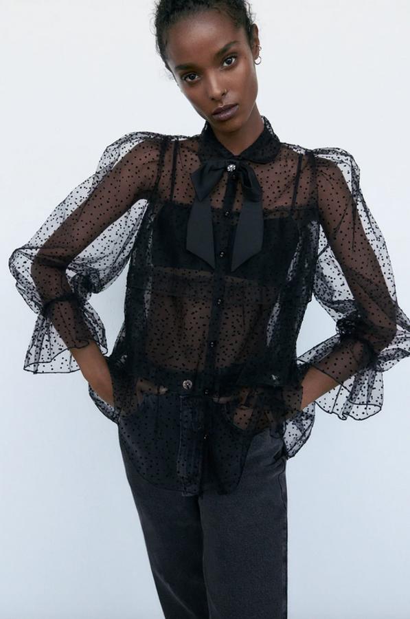 De cuello solapa con lazo y manga larga, esta blusa semitransparente de Zara en plumeti viene con detalle de volantes a tono y cierre frontal de botones. Podemos encontrarla entre las tallas XS y L por 25,95 euros.
