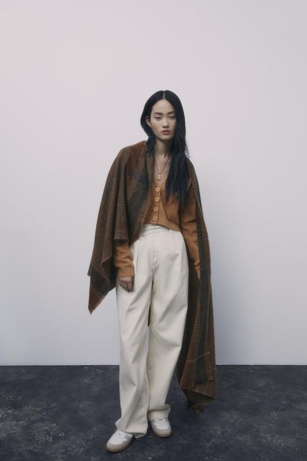 Manta de cuadros escoceses a modo de capa sobre rebeca de lana corta y pantalones de talle alto, todo de Zara.