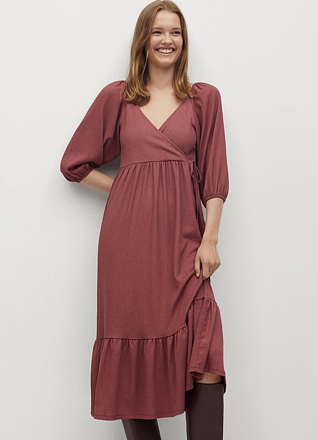 Este vestido midi de color granate y diseño acampanado cuenta con escote cruzado y manga corta abullonada. Con volante en el bajo y cierre de lazo lateral, es de Mango y tiene un precio rebajado de 19,99 euros.