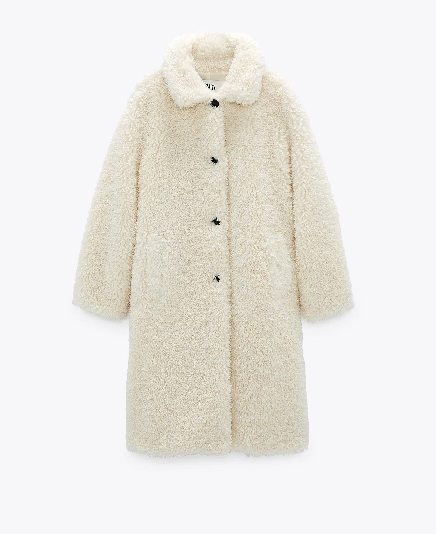 Abrigo largo de cuello solapa en blanco crudo, textura de borreguito, cierre de botones delanteros y bolsillos. De la nueva colección de Zara. (79,95 euros).