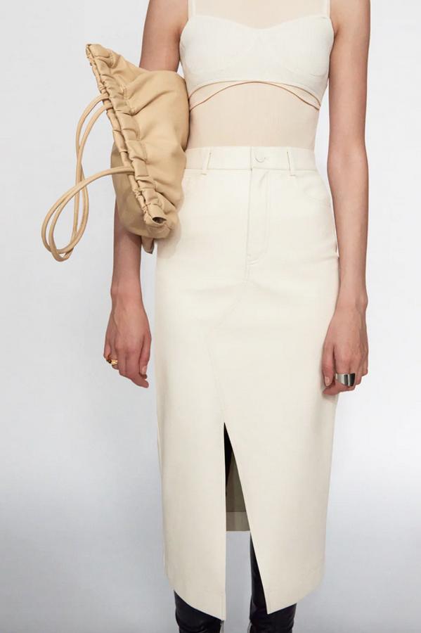 En color crudo, con diseño midi de tiro alto, cinco bolsillos, bajo con abertura en delantero y cierre frontal de cremallera y botón para esta falda de Zara en efecto piel que cuesta 25,95 euros y está disponible entre las tallas XS y XL.