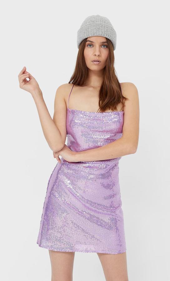 Este vestido en color violeta es de Pull&Bear y está confeccionado en tejido brillante con escote de pico cruzado, falda tipo pareo con volantes y mangas largas. Está disponible entre las tallas XS y L por 19,99 euros.