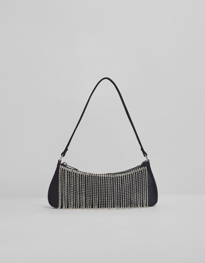 En color negro con detalle de cadenas de strass en el frontal, asa corta y formato baguette, este bolso de Bershka costaba 17,99 euros y ahora está por 9,99 euros.