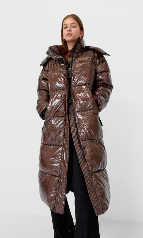 Este abrigo largo acolchado en color marrón y acharolado es de Stradivarius y viene con cuello subido, capucha y cierre frontal de cremallera y botones de clip oculto. De 59,99 euros ha pasado a costar 49,99 euros y solo queda en la talla M.