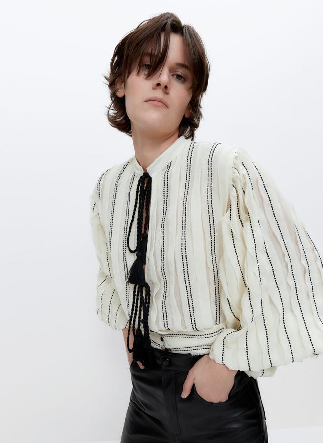 Con cuello mao, en color crudo con rayas negras bordadas y manga abullonada, esta camisa con cintura tipo fajín viene con cierre frontal con tapeta, botones forrados y cordones con pompones en el cuello. De 89 euros ha pasado a 59,95 euros y está disponible en las tallas XS, S y M.