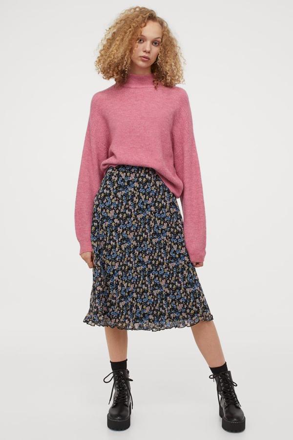 De fondo negro con estampado floral en azul y rosa claro, esta falda plisada en tejido vaporoso de gasa con cintura estándar elástica y largo hasta la rodilla. Tiene un precio de 19,99 euros y está disponible entre las tallas XS y XL.