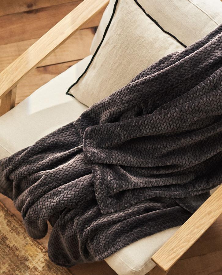 Disponible en cruzo o en gris oscuro, esta manta con superficie suave y efecto trenzado mide 140x190 centímetros y tiene un precio de 29,99 euros.