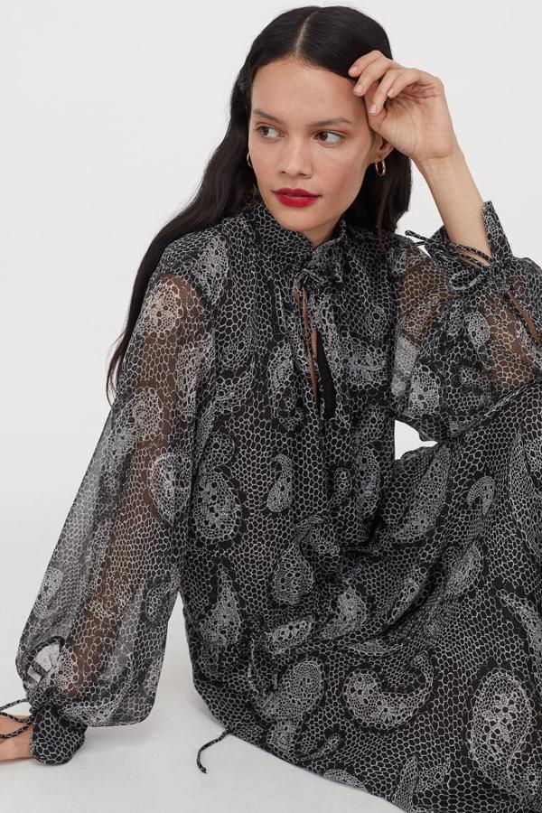 Este vestido negro con estampado paisley confeccionado en tejido vaporoso con silueta evasé viene con cuello elevado de doble capa, abertura en el escote con cordón de ajuste superior y hombros ligeramente caídos. Con mangas globo y costura asimétrica en las caderas, la falda tiene volumen y suave caída. Podemos encontrarlo en las tallas XS, S y L por 49,99 euros.