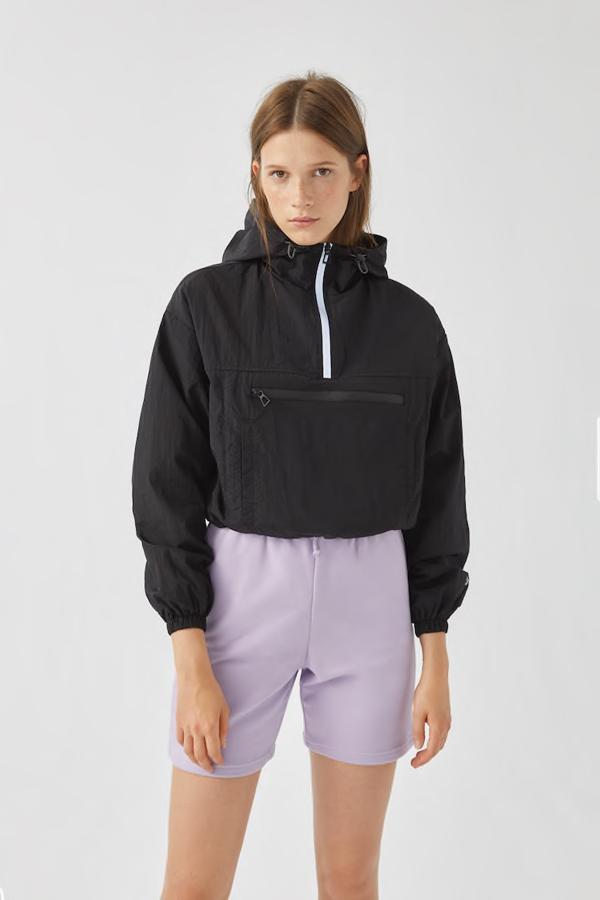 Cazadora canguro corta confeccionada en nailon, de manga larga, con capucha, bolsillo delantero y cierre mediante cremallera hasta el pecho, de las rebajas de Pull & Bear (9,99 €).