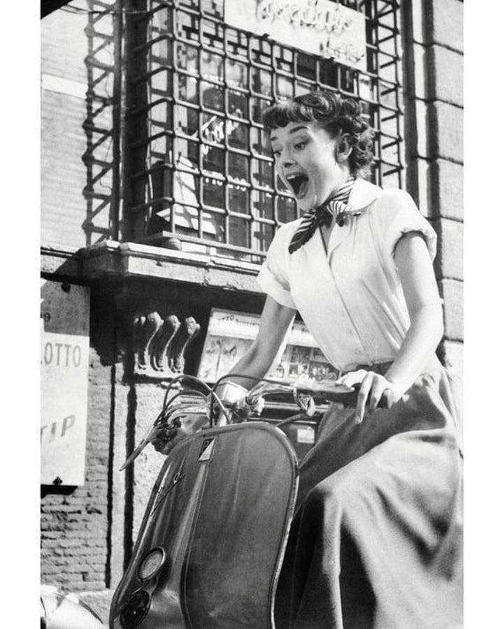 ‘Vacaciones en Roma’. Por su culpa (o gracias a ella) muchas hemos querido recorrer las calles empedradas de la ciudad eterna en Vespino y con un pañuelo anudado al cuello. La blusa blanca ligeramente remangada es un acierto seguro y la falda midi, un básico que casi todas tenemos actualmente en nuestro armario.