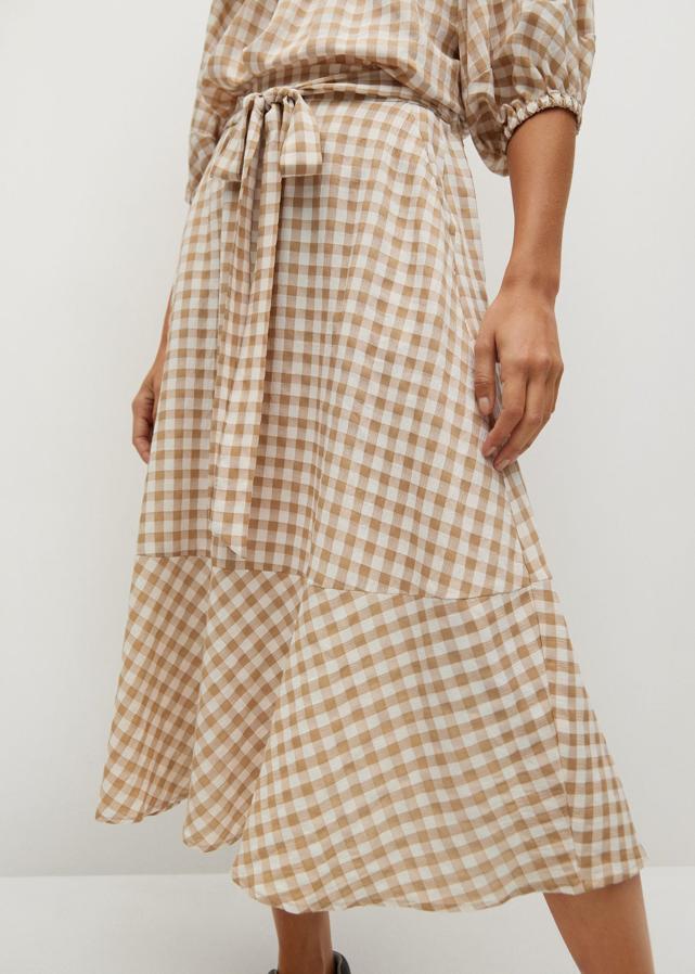 Con estampado de cuadros en beige, esta falda de Mango con diseño midi acampanado tiene cintura elástica con cinturón ajustable con lazo y volante en el bajo. Podemos encontrarla entre las tallas XS y L por 29,99 euros.