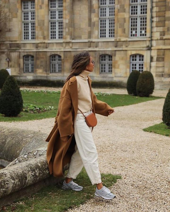 Abrigo oversize de color camel + pantalón blanco de corte "mom" + jersey de cuello alto color arena + zapatillas New Balance