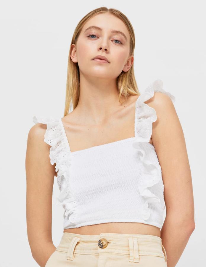 Top corto con escote cuadrado, sin mangas y detalles de volantes en tirantes y cuello. Elásticos en los laterales tipo nido de abeja y cordón en la espalda. Precio actual: 15,99 euros.