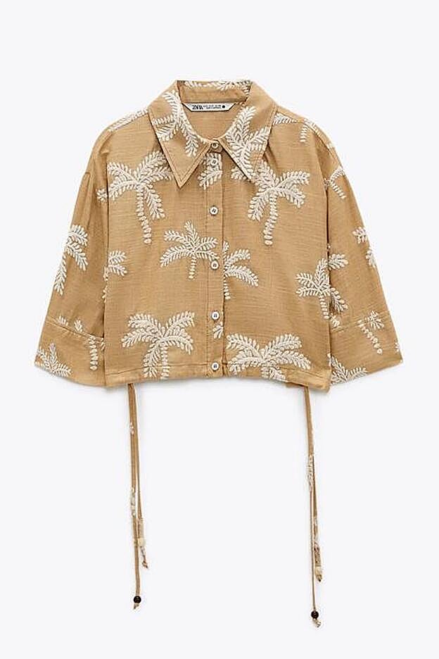 Esta blusa corta, confeccionada en lino en color ocre y con palmeras bordadas, pretende ser una prenda protagonista y combinar con todo.