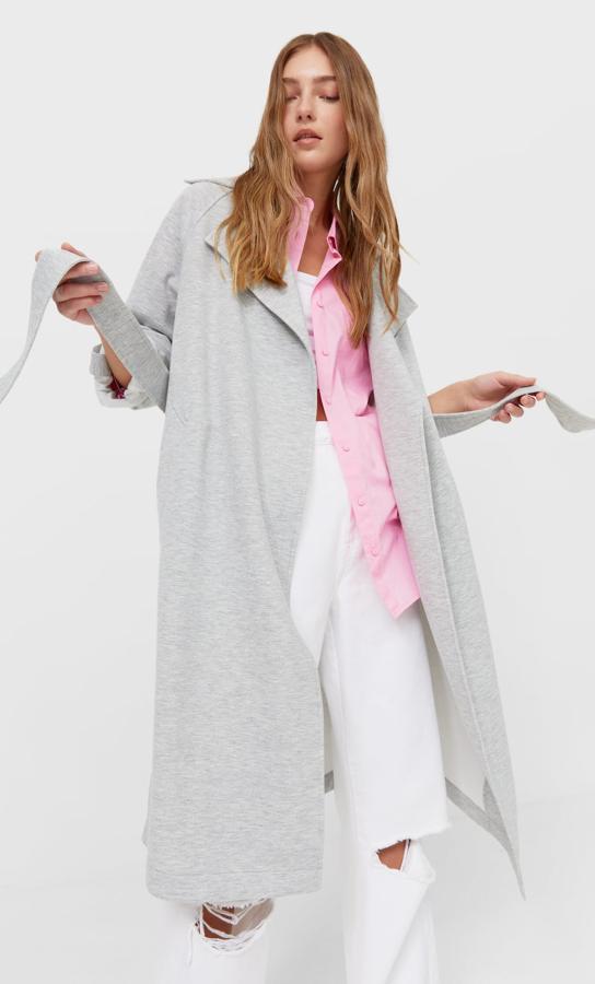 Este trench fluido con solapa y cinturón del mismo tejido está disponible en gris o beige. Tiene un precio de 35,99 euros.