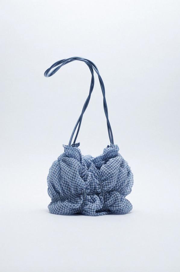 En formato saca, con cuerpo fruncido con cuadro Vichy en azul y blanco, este bolso de Zara confeccionado en organza viene con asas de hombro a tono, interior forrado y cierre de imán, cuesta 19,95 euros.