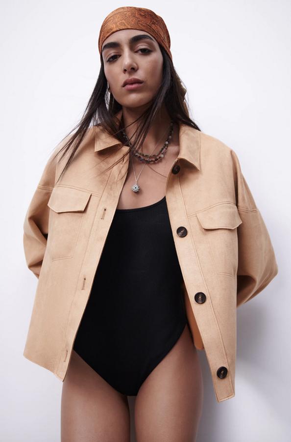 De diseño cropped y en efecto ante, esta sobrecamisa de color tostado de Zara viene con cuello de solapa y bolsillos delanteros de plastrón con solapa sin botón. Con cierre de botones frontal a contraste, cuesta 25,95 euros y está disponible entre las tallas XS y XXL.