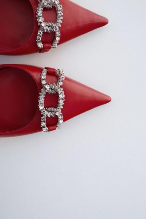 Zapato de tacón destalonado de piel en color rojo. Detalle de eslabones en plata envejecida y joya en la parte delantera. Tira con elástico en la parte trasera. Son de Zara. Precio: 49,95 euros.