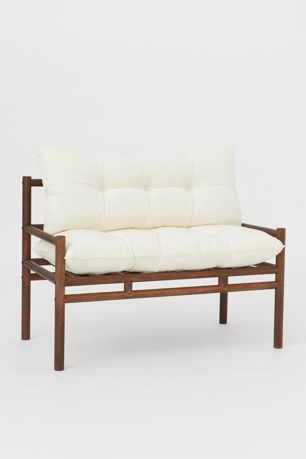 En madera meranti de color marrón, este banco con respaldo en sarga y cojines blancos tiene un ancho de 57 centímetros, una altura de 76 y un largo de 108. Tiene un precio de 299 euros.
