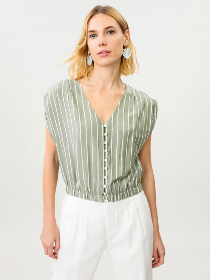 En color verde con rayas, esta camisa corta con goma elástica en el bajo y escote de pico cuenta con fruncidos en los hombres y cierre mediante botones frontales. Tiene un precio de 12,99 euros.