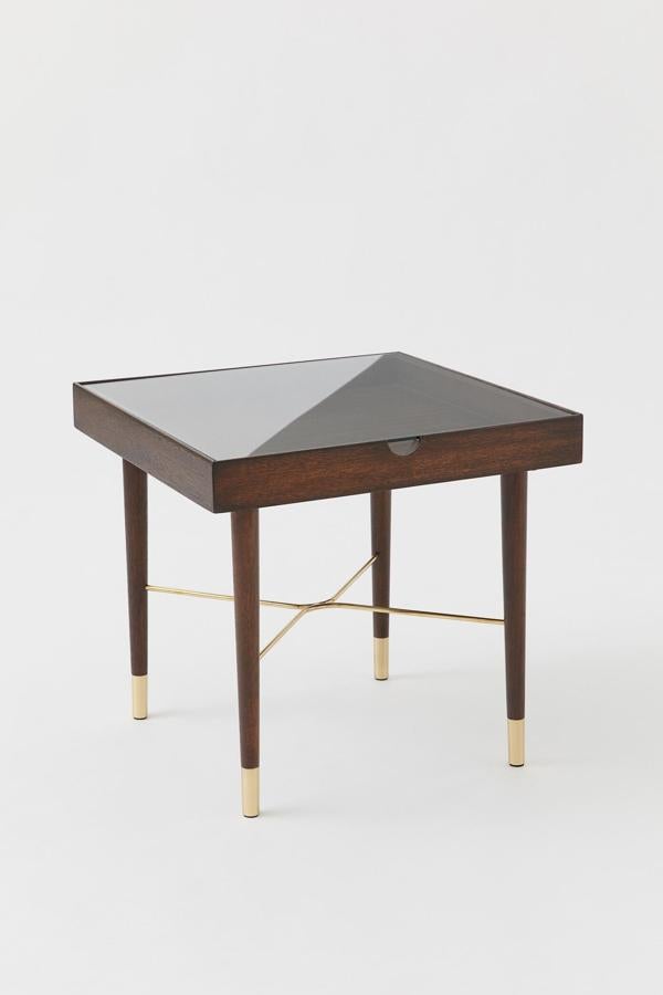 Disponible en marrón oscuro o negro, esta mesa auxiliar de madera y metal cuenta con un tablero de vidrio elevable que permite almacenar cosas en su interior. Tiene un precio de 179 euros.