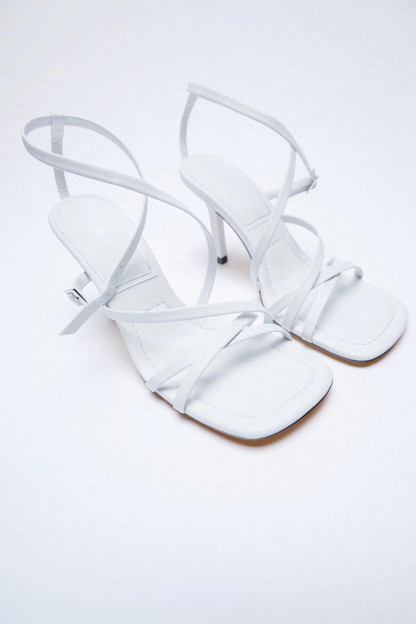 Sandalias blancas de Zara con tacón alto de 10 centímetros, tiras finas de piel, suela cuadrada super cómoda y cierre de hebilla. (39,95 euros).