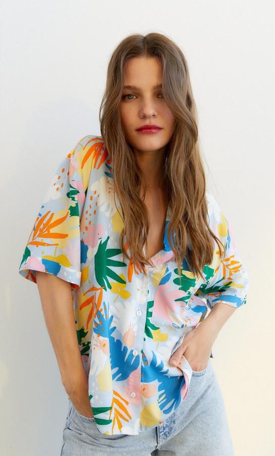Con estampado de motivos tropicales en tonos rosas, azules, verdes y amarillos, esta camisa de manga corta de Stradivarius con cuello y solapa, escote de pico y bolsillo de plastrón en la pechera tiene un precio de 15,99 euros y está disponible entre las tallas XS y XL.