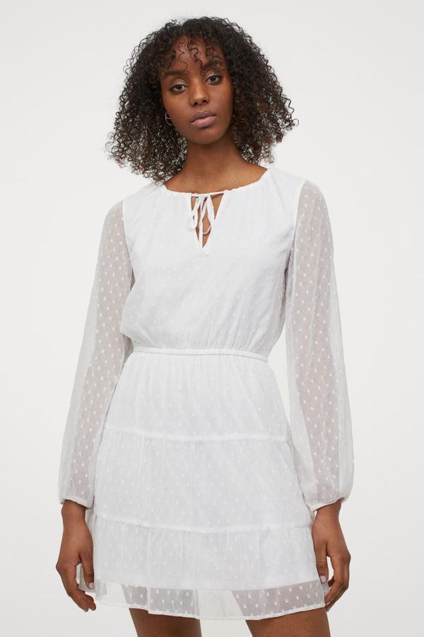 Diseño corto en gasa arrugada con plumeti para este vestido blanco de H&M con cuello redondo con cordón de ajuste y tiras de anudar, mangas largas amplias acabadas en elástico fino en los puños y fruncido escalonado con vuelo en la falda. Cuesta 19,99 euros y podemos encontrarlo entre las tallas 40 y 50, aunque muchas de ellas se están agotando.