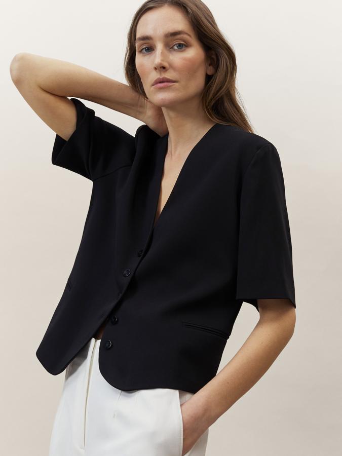 De corte recto, con cuello de pico y cierre de botones frontal a tono, esta chaqueta corta de Massimo Dutti en color negro viene con dos bolsillos de ojal y mangas cortas. Disponible entre las tallas XS y L por 69,95 euros.
